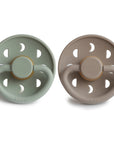 Two Frigg Moon Rubber baby pacifiers, one Sage and one Portobello, on a white background.