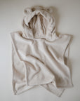 The mushie Bear Poncho Towel, made from organic cotton in light beige, is spread out on a white surface. Its hood has two small, rounded fabric ears for a cute, bear-like look.