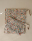 Two mushie Water Resistant Wet Bags with zippers and ribbon loops, featuring a floral design in orange and green, are placed on a neutral surface—ideal for diaper bag storage.