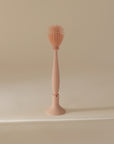 The mushie Silicone Baby Bottle Brush, featuring silicone bristles and a textured spiky head, stands upright on its matching base against a plain beige background.