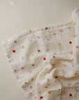 The mushie Organic Cotton Muslin Swaddle Blanket features soft white crinkled fabric with scattered colorful circles and smiley faces, perfect for gently wrapping your baby in comfort.