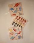 Mushie's Wooden Space Puzzle with dinosaur and alphabet puzzles on a beige surface.