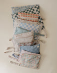 A selection of mushie Water Resistant Wet Bags, featuring zipper closures and side straps, is neatly displayed. These stylish wet bags come in floral, checked, and geometric prints—perfect for organized diaper bag storage.