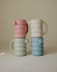 Four stackable Mushie Silicone Watering cans in pastel colors, two with a confetti pattern.
