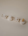 The FRIGG Baby's First Pacifier Moonlight Sailing (Cream) 4-Pack, by FRIGG, features four cream pacifiers in various shapes with silicone nipples, neatly arranged on a light beige surface.
