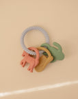 The mushie Western Teething Ring is made from food grade silicone in pink, yellow, and green, shown on a light beige background.