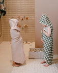 Two kids in hooded towels stand by a mushie Diaper Caddy in the bathroom.