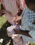 Two kids hold a mushie Silicone Sensory Toy while standing on grass near daisies.