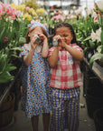 Two kids play with mushie Kaleidoscopes among flowers in a greenhouse.