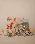 A selection of pastel Mushie baby toys, including a wooden alphabet puzzle to encourage fine motor skills, animal puzzles, a sun rattle, cloud shapes, a sippy cup, and pacifiers—all displayed against a neutral backdrop.