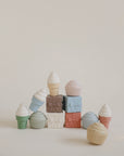 A pyramid of pastel mushie Mix and Match Ice Cream Toys sits against a plain background. The white-topped silicone treats, some with sprinkles, encourage fine motor skill development while inspiring creative play.
