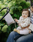 A parent holds a baby near a stroller with a mushie Water Resistant Wet Bag on the handle.