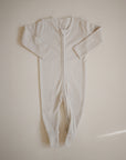 The mushie Zipper Pajama is a cream-colored, long-sleeve baby onesie with footed legs and a front zipper, made from cozy organic cotton. It is shown laid flat on a neutral background.