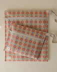 The mushie Water Resistant Wet Bag includes two zipper pouches with wrist straps, featuring a retro floral design in orange, blue, yellow, and pink on beige—ideal for diaper bag storage.