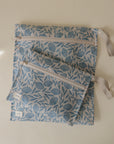 Two light blue mushie Water Resistant Wet Bags with floral designs and beige straps rest on a neutral surface. The larger bag is underneath the smaller, both featuring white tags on their seams.
