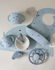 The mushie Snack Cup is a light blue silicone snack cup for toddlers, decorated with colorful tiny car patterns to delight little ones.