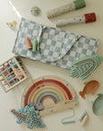 Mushie Silicone Sensory Toy with baby toys, a checkered bag, and pacifiers on light surface.