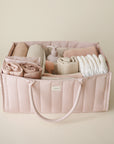 Lifestyle image of the Blush Diaper Caddy with folded clothes and baby nursery items on a beige background.