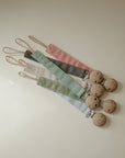 Mushie Linen Pacifier Clip 2-Pack: 4 wooden holders with pastel clips in pink, cream, green, blue.