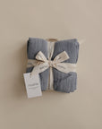 A neatly folded mushie Organic Cotton Muslin Cloths 3-Pack, tied with a cream ribbon, sits on a neutral background. A white tag reads “mushie”—perfect for nursery use or keeping handy in the diaper bag.