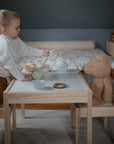 A young child enjoys a pretend tea party with a teddy bear and their favorite FRIGG Baby's First Pacifier Moonlight Sailing (Powder Blue) 4-Pack by FRIGG, made in Denmark, resting nearby in the cozy room.