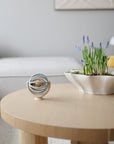 Round wooden coffee table with decorative items including a bowl of plants and a mushie suction spinner ball toy in a living room setting.