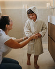 A woman smiles at a child in a mushie Bear Robe in the bathroom.