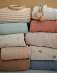 Extra soft mushie muslin crib sheet with wooden pacifier clips stacked on top.
