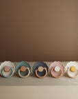 The FRIGG Daisy Silicone Pacifier 2-Pack by FRIGG features medical-grade silicone, round handles, and scalloped edges in soothing pastel colors, shown arranged neatly on a neutral background.