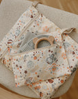 A mushie Water Resistant Wet Bag with space-themed patterns and zippers sits open on a beige chair, showing a textured cloth and bear-ear teether inside—ideal for storing diaper bag essentials.