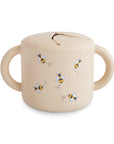 The mushie Snack Cup is a beige silicone cup with two handles and a flexible, spill-proof lid, featuring adorable bee illustrations—perfectly sized for toddlers’ hands.