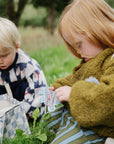 Two kids on grass, one playing with a mushie Silicone Sensory Toy in their hand.