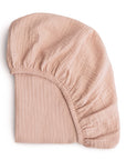The mushie Extra Soft Bassinet Muslin Crib Sheet is shown folded, with elastic edges and its light pink, breathable texture visible against a white background.