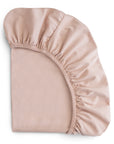 A neatly folded light pink mushie Stretchy Bassinet Sheet displays its elastic edge and gathered fabric at one corner.