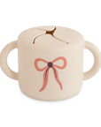 Mushie Snack Cup, Bows color, spill-proof with handles—perfect for toddlers.