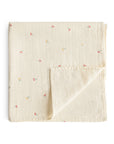 Mushie Organic Cotton Muslin Swaddle Blanket in cream with small florals, folded on white.