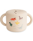 The mushie Snack Cup in Dinosaurs features a spill-proof lid, two handles, and colorful cartoon dinosaurs with dotted footprints. A perfect toddler snack container!.