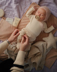 An adult applies mushie Baby Cream to a baby with dry skin, who is holding a pacifier.