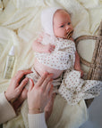 Baby in a basket as someone applies mushie Baby Oil to their belly, wearing a hat and pacifier.