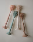 The mushie Silicone Baby Bottle Brush set includes four pastel-colored brushes (peach, cream, green, beige) with long handles and silicone bristles, arranged in a fan shape—ideal for cleaning bottles and nipples.
