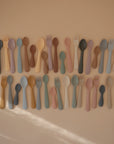 Rows of colorful mushie Dinnerware Fork and Spoon Sets on a beige background.