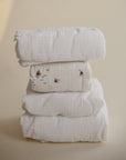 A stack of four mushie Extra Soft Muslin Crib Sheets, one with small sailboat prints.