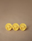 Two FRIGG Rope/Daisy Natural Rubber Pacifiers in Sunflower and Fuchsia (6-18 Months) are displayed on a light brown background—a perfect, stylish addition to your baby essentials.