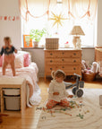 Two kids play in a bright room; a mushie Mini Toddler Bike sits among their scattered toys.