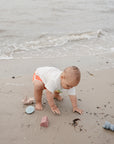 Lifestyle image of a baby playing on a sandy beach with the mushie Pirate Bath Play Set.
