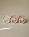 FRIGG Daisy Night Natural Rubber Pacifiers, 2-pack, displayed on a beige surface.