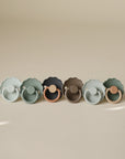 Six FRIGG Daisy Natural Rubber Pacifiers (3 packs of 2) lined up on a beige surface.
