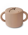 The mushie Snack Cup in Natural is a round silicone cup with two handles and a flexible, slit opening, designed to prevent spills and allow easy snack access.