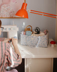 Person organizing supplies in a mushie Diaper Caddy under an orange lamp.