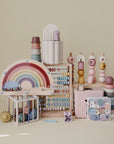 A pastel display of children’s toys, featuring the mushie Wooden Magnetic Rainbow Maze, stacking rings, abacuses, beads, and geometric shapes—all perfect for screen-free fun and developing fine motor skills.